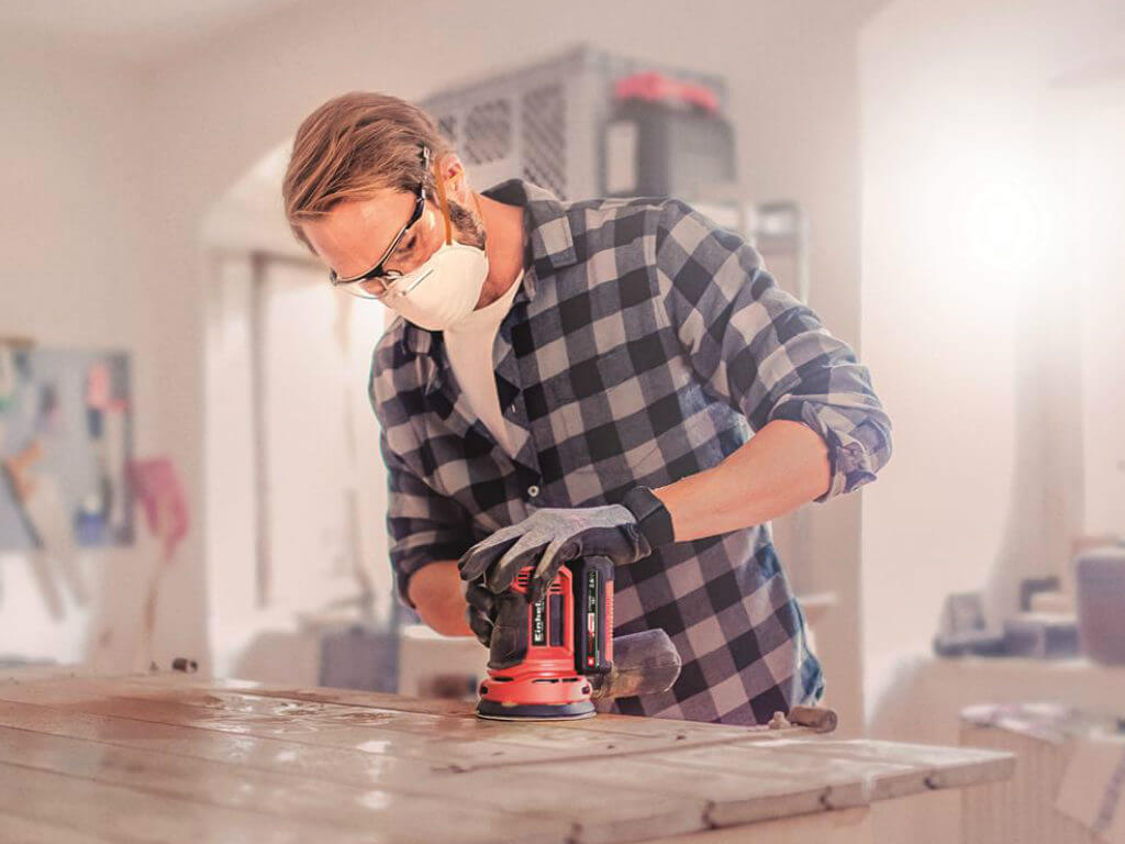 man working with cordless rotating sander in a workshop