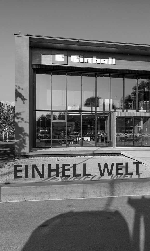 Black-and-white image of the Einhell world: modern company building with Einhell logo and large group of employees.