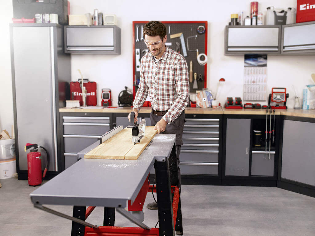 man cuts wooden board in two parts with a table saw