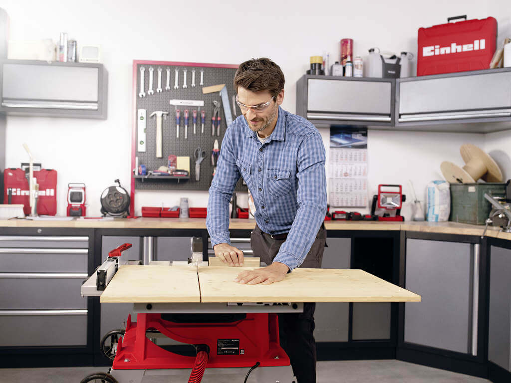 man cuts wooden board in two parts with a table saw