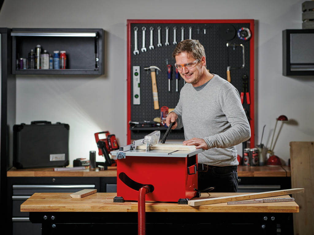 man cuts wooden board in two parts with a table saw