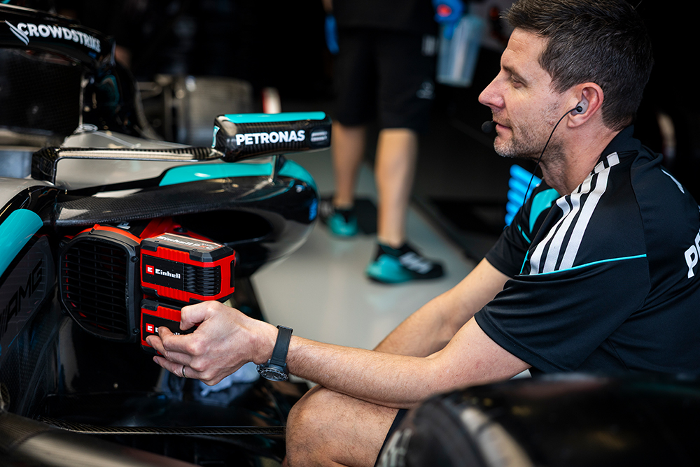 Formula 1 mechanic working with a tool on a race car in the pit.