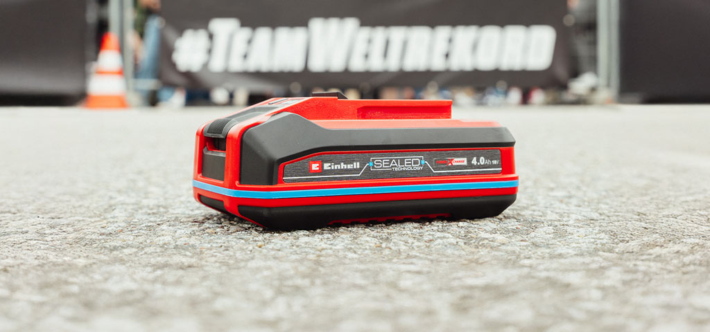 Einhell Power X-Change 4.0 Ah SEALED battery displayed in front of a Team Weltrekord banner