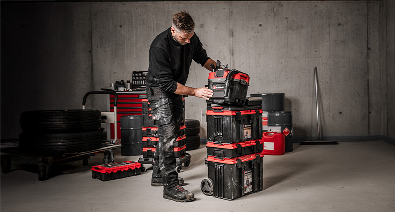 Ein Mann stellt einen kleineren Einhell Koffer auf ein hohes, rollbares E-Case System mit mehreren Modulen.